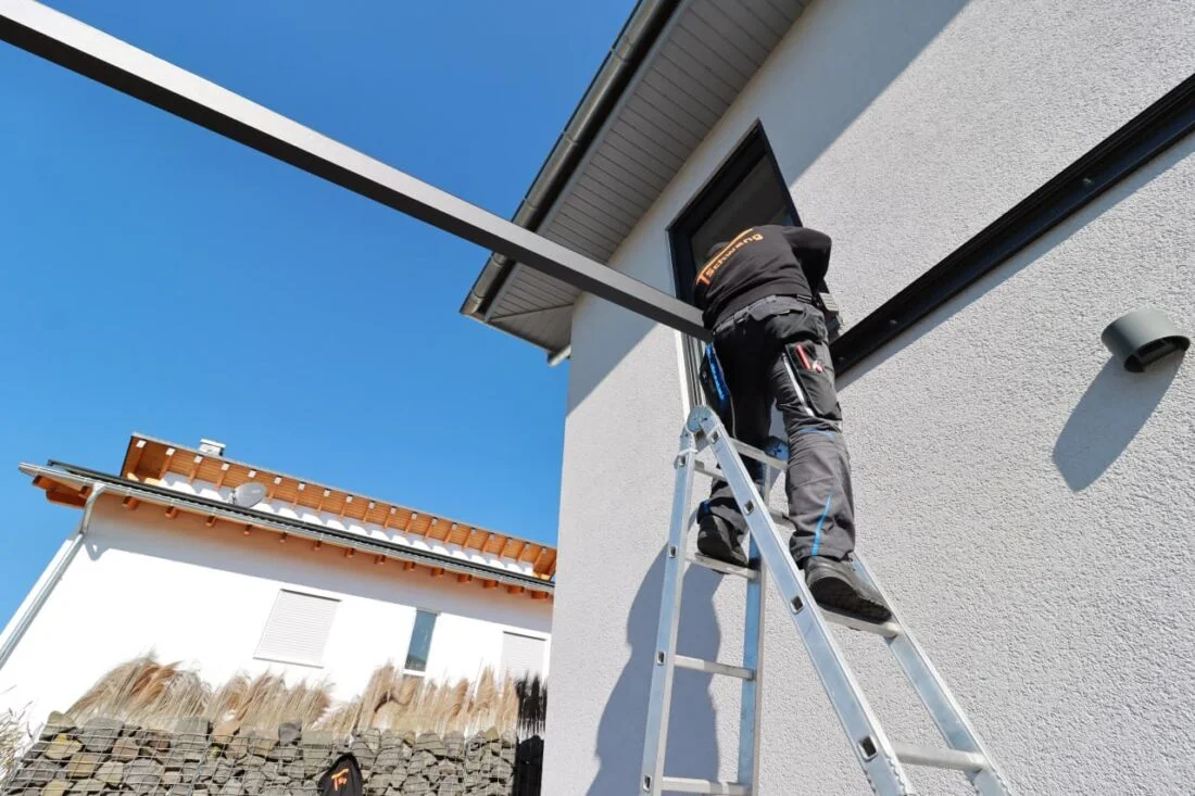 Строитель на лестнице монтирует алюминиевые трубы