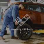 Мужчина в синей рабочей форме меняет колесо красного автомобиля в автосервисе. Логотип WILS